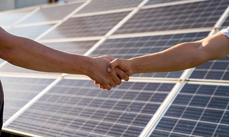 Two men shaking hands in front of solar panels